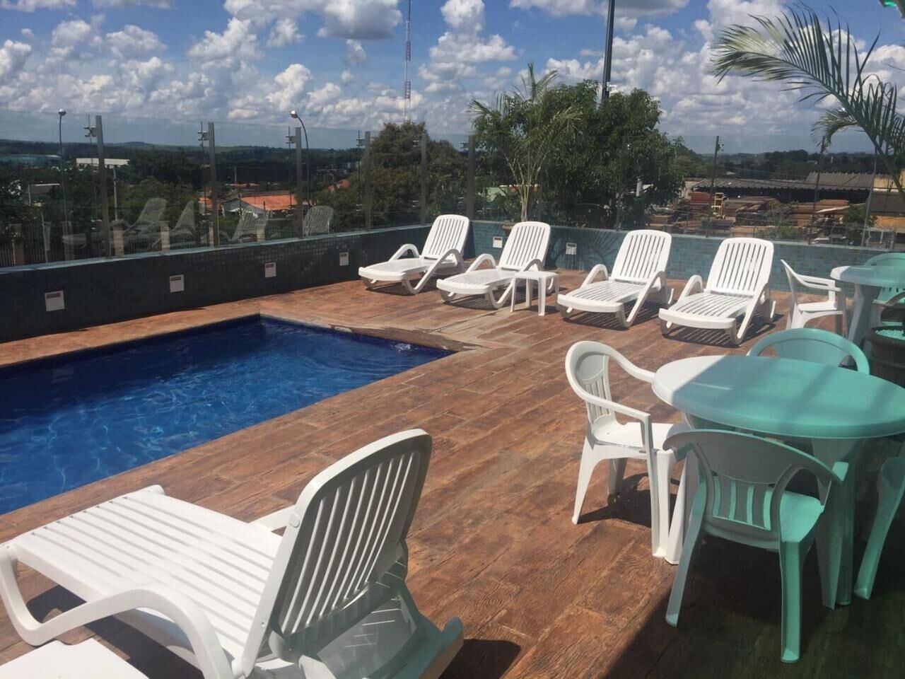 A rooftop pool area with lounge chairs and tables, surrounded by a wooden deck and a view of the cityscape.