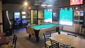 Una sala de billar con mesa de billar, sillas y máquinas de juegos.