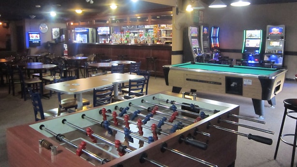 Zona de bar con mesa de fútbol de mesa, mesa de billar y varias máquinas de juego.