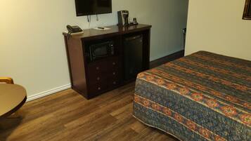 A hotel room with a wooden floor, a bed with a patterned bedspread, a desk with a telephone and a coffee maker, and a TV mounted on the wall.