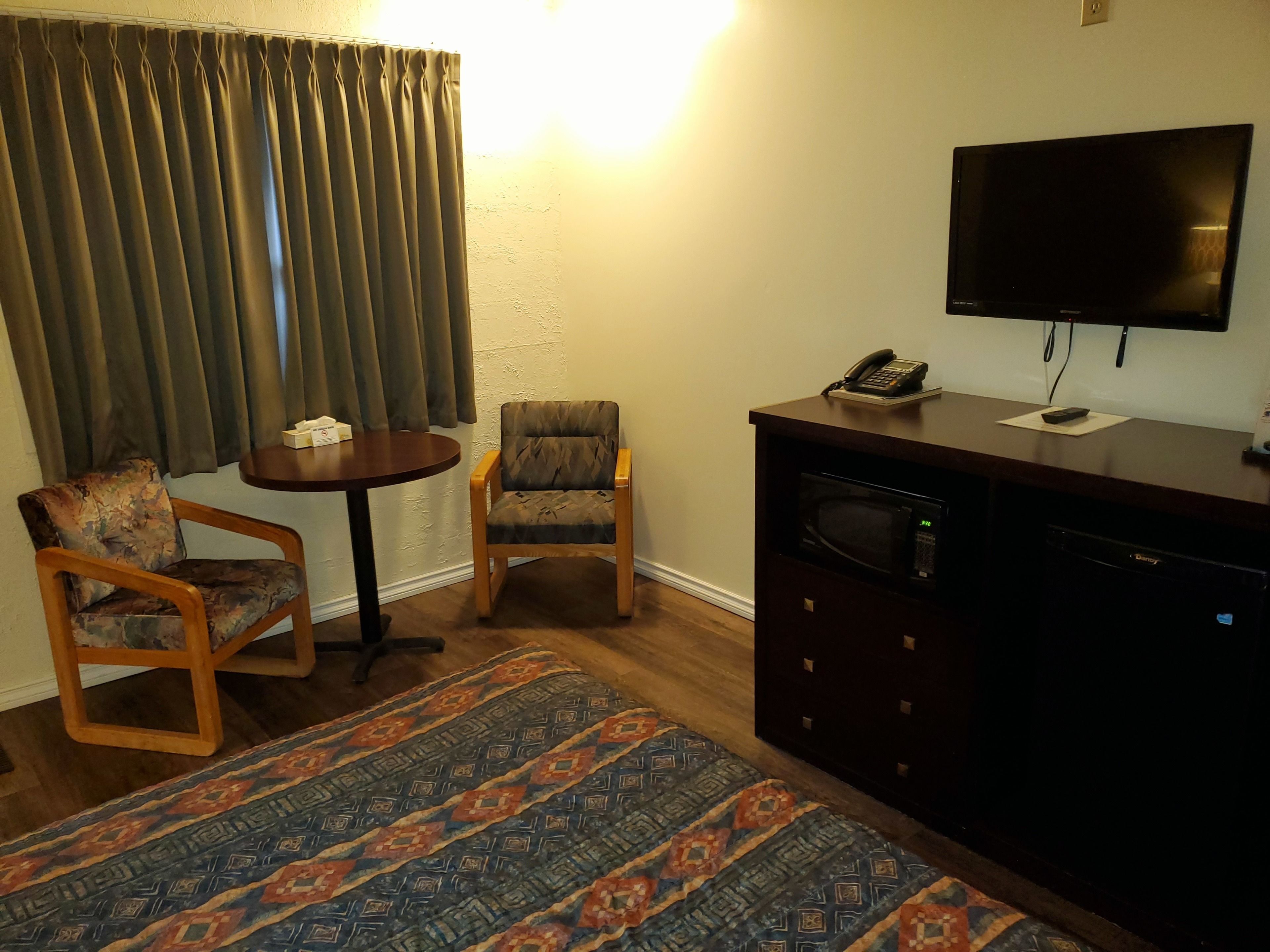 Una habitación pequeña y acogedora con televisión de pantalla plana en la pared, microondas y una mesita con una silla.