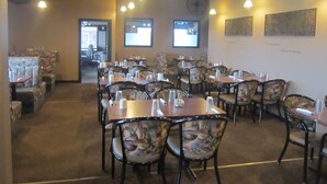 Un restaurante con varias mesas y sillas, un reloj en la pared y obras de arte enmarcadas.