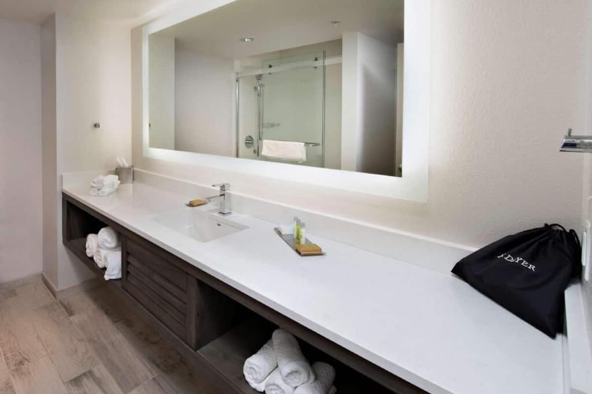 A modern bathroom with a large mirror, a sink, and a shower. There are towels and toiletries on the counter.