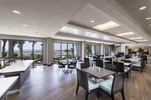 Un comedor amplio e interior con varias mesas y sillas, ventanas grandes que ofrecen vistas al exterior, y un diseño de techo moderno.