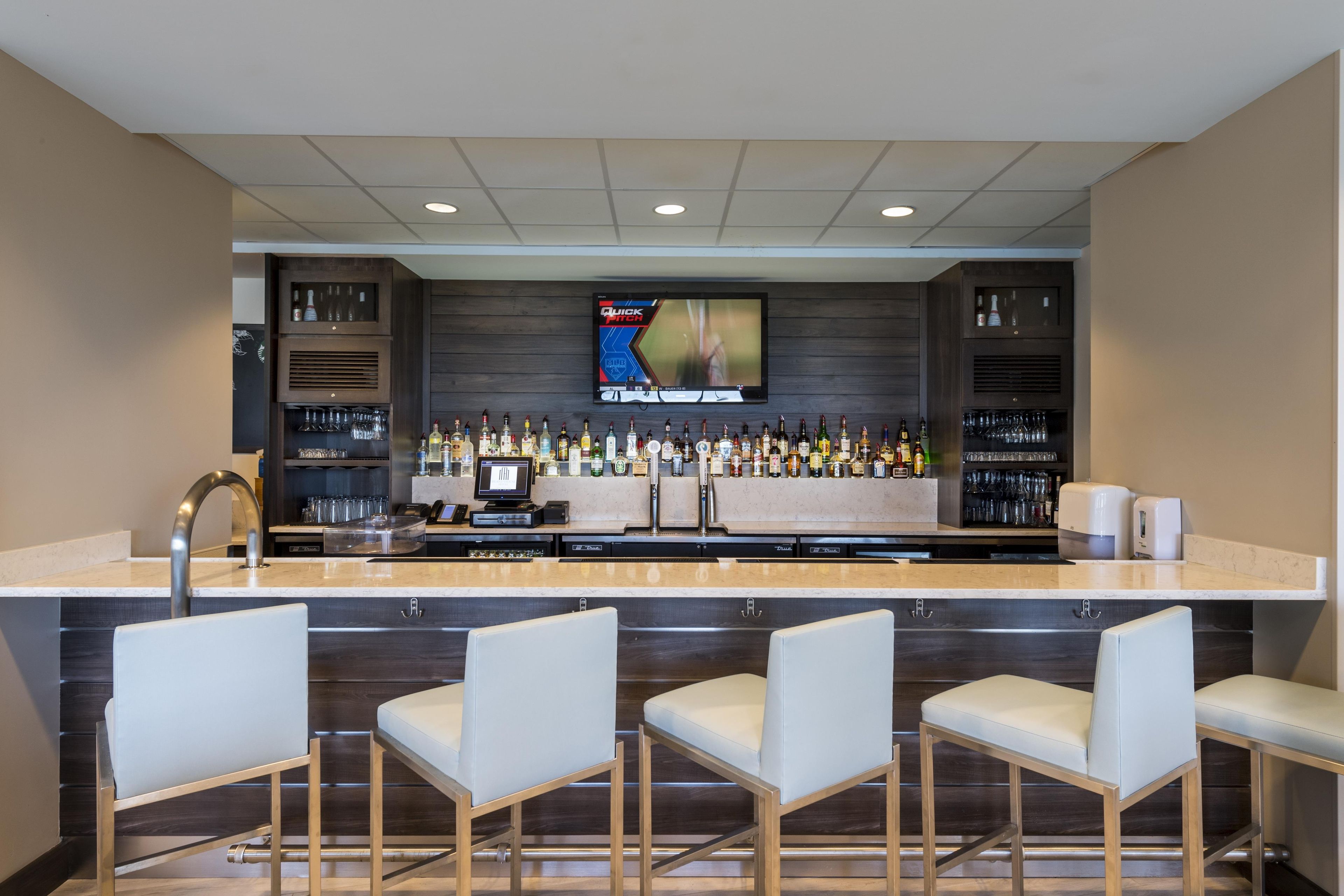 A bar area with a flat-screen TV, bar stools, and a variety of liquor bottles.
