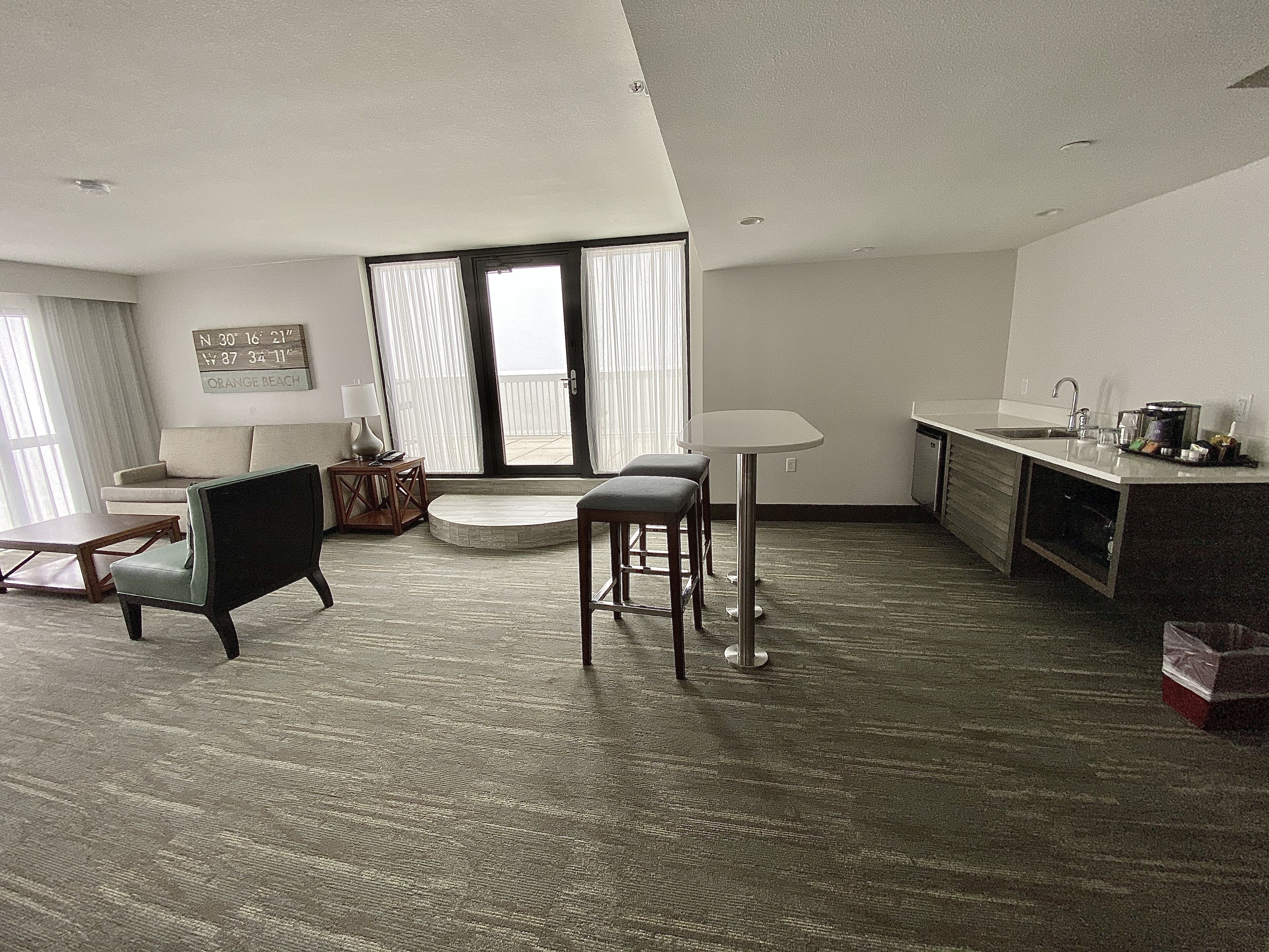 A modern living room with a sofa, two chairs, a coffee table, and a dining area with a table and bar stools.