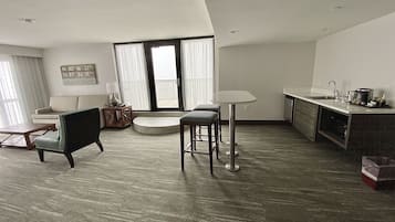 A modern living room with a sofa, two chairs, a coffee table, and a dining area with a table and bar stools.