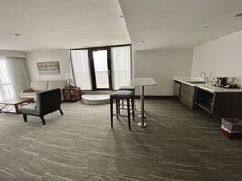A modern living room with a sofa, two chairs, a coffee table, and a dining area with a table and bar stools.