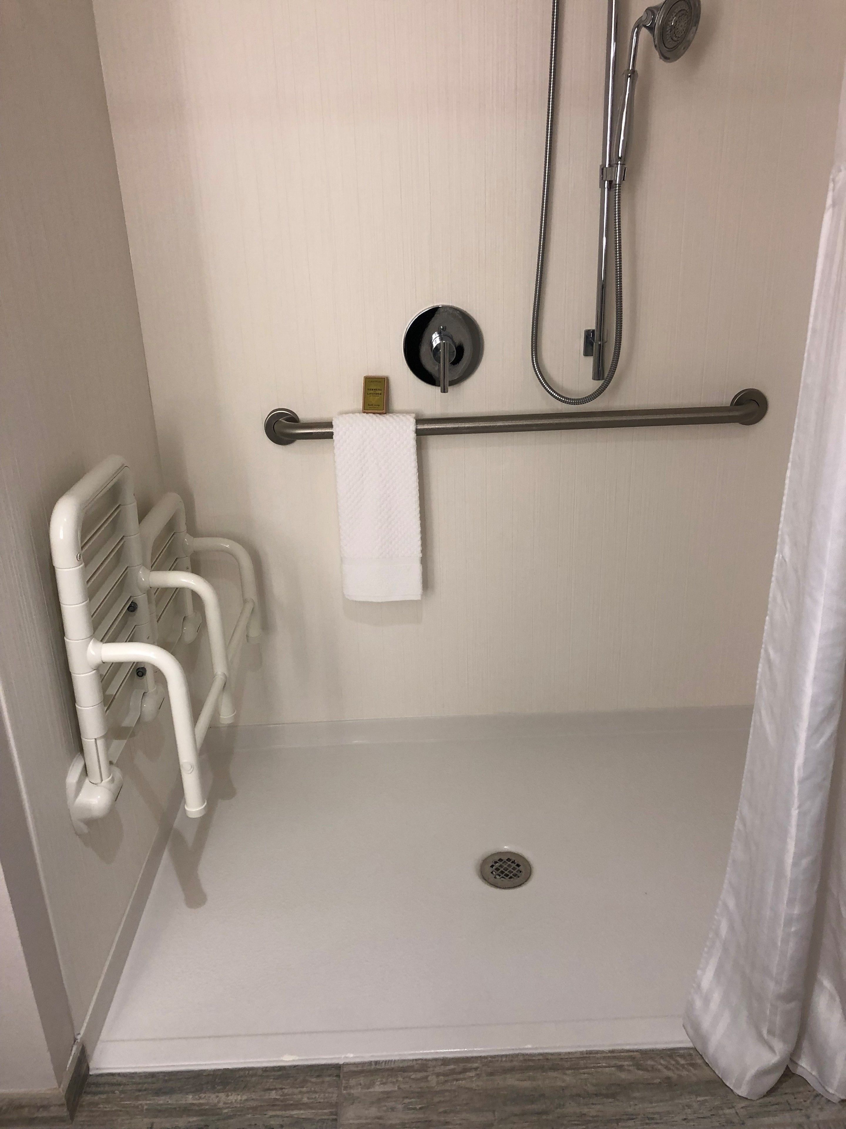 A shower area with a grab bar, a towel rack, and a handheld showerhead.
