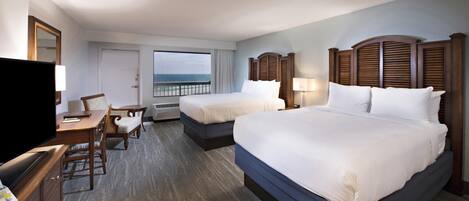 A hotel room with two beds, a desk, a chair, a TV, and a view of the ocean.