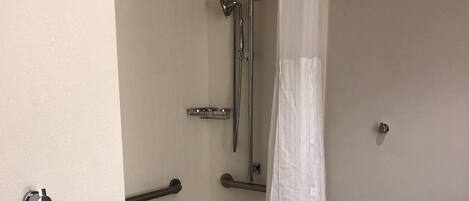 Baño con bañera, ducha y barras de apoyo.