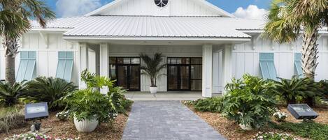 A white building with a central entrance, flanked by potted plants and a paved walkway.
