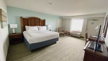 Ein Hotelzimmer mit einem großen Bett, einem Schreibtisch, einem Stuhl, einem kleinen Tisch und einem Fenster mit Vorhängen.