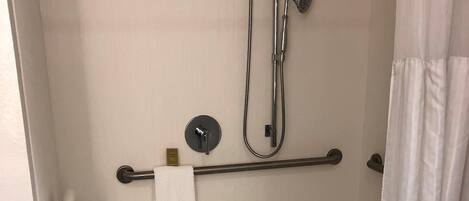 A walk-in shower with a grab bar, a towel rack, and a showerhead.