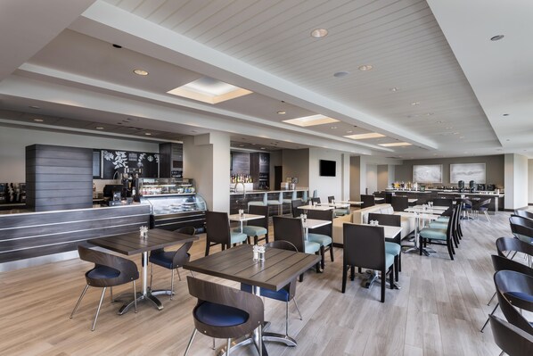 A modern restaurant with multiple dining areas, a bar, and a kitchen visible in the background.