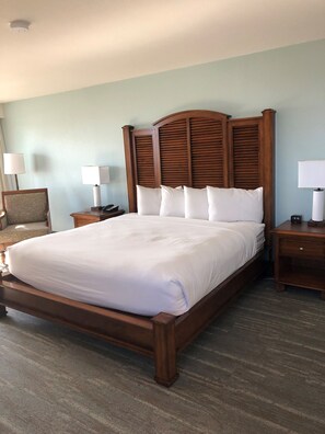 Una habitación de hotel con una cama grande, cabecera de madera, dos mesitas de noche y una silla.