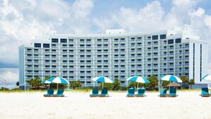 A large hotel with multiple balconies, beach chairs with umbrellas, and a flag. - Island House Hotel Orange Beach - a DoubleTree by Hilton (Orange Beach)