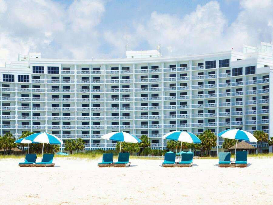 Un grand hôtel doté de nombreux balcons, de chaises de plage avec des parasols et d’un drapeau.