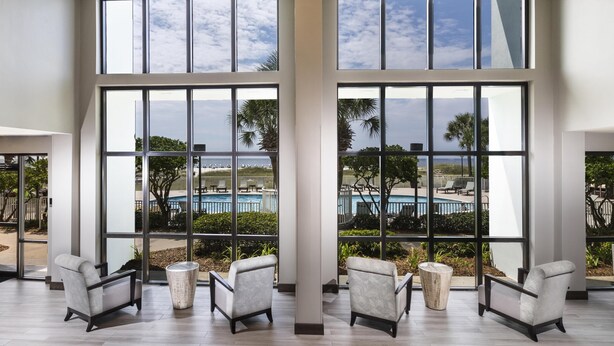 A spacious room with large windows, a pool view, and modern furniture. - Island House Hotel Orange Beach - a DoubleTree by Hilton (Orange Beach)