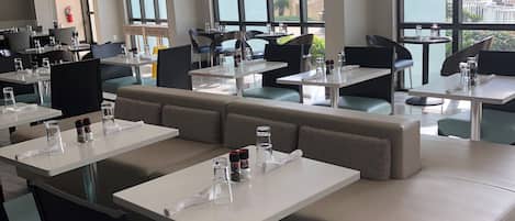 Et moderne restaurantmiljø med høje borde, polstrede siddepladser og store vinduer med udsigt.