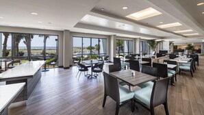 A spacious indoor dining area with large windows, multiple tables, and chairs. - Island House Hotel Orange Beach - a DoubleTree by Hilton (Orange Beach)