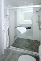 A modern bathroom with a glass-enclosed shower, a white toilet, and a robe hanging on a hook.