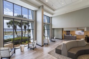 A spacious lobby with large windows, a reception desk, and a seating area with a view of the pool and palm trees.