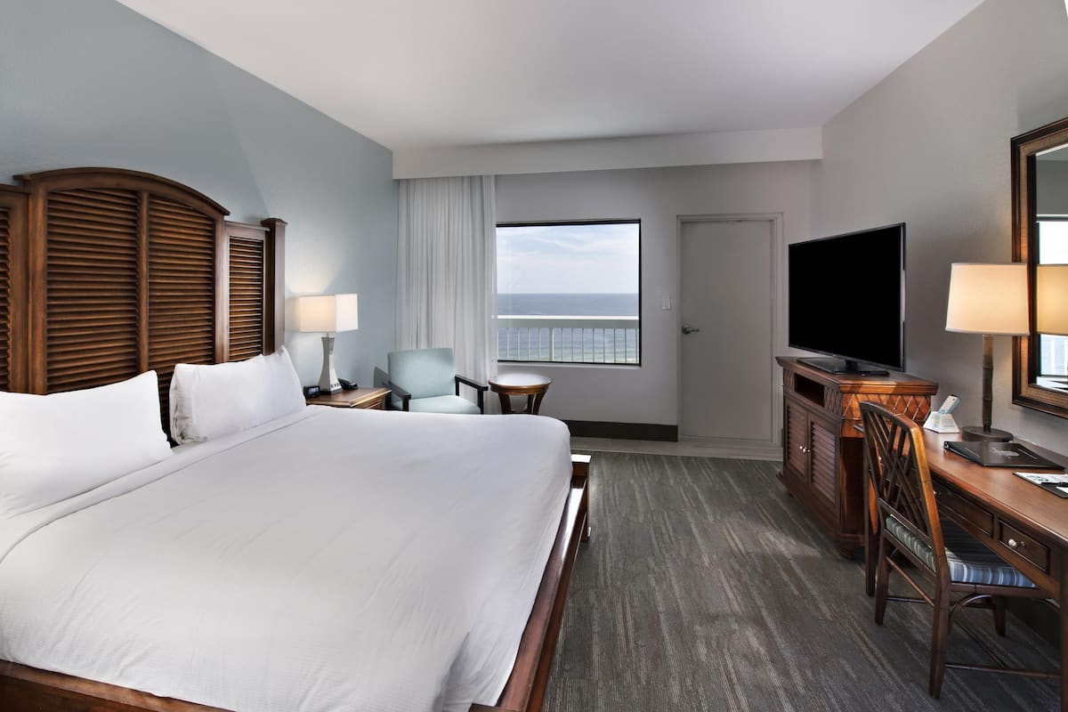 A hotel room with a large bed, a desk with a television, a chair, and a window with a view.