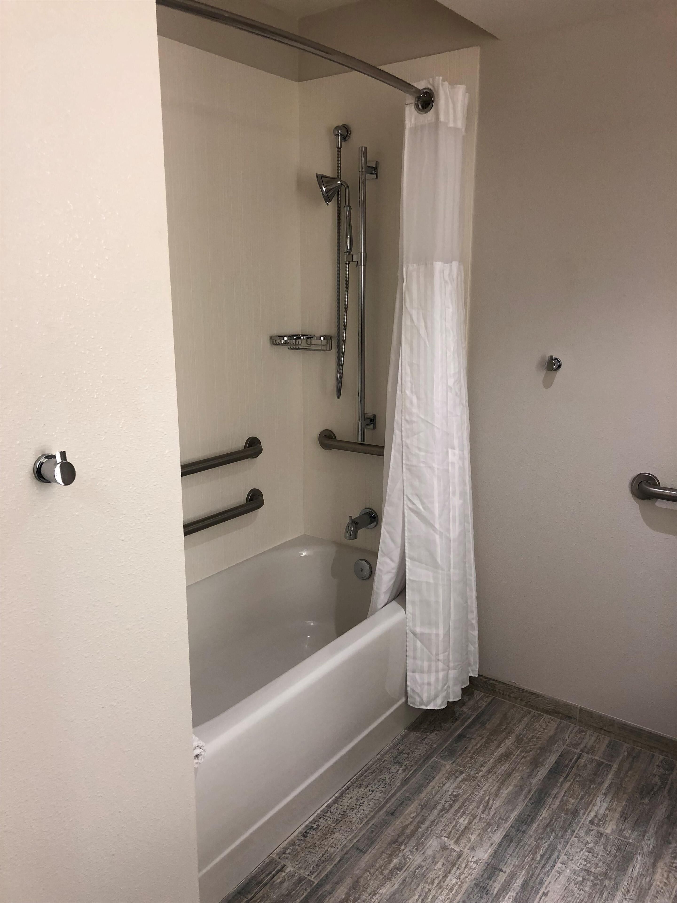 A bathroom with a bathtub, shower, and grab bars.