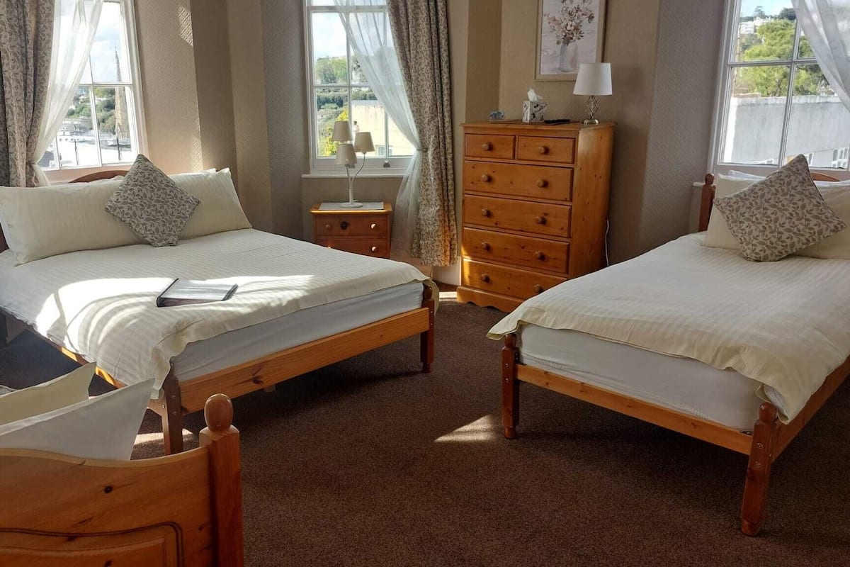 A bedroom with two wooden beds, a wooden dresser, a nightstand, and a window with curtains.