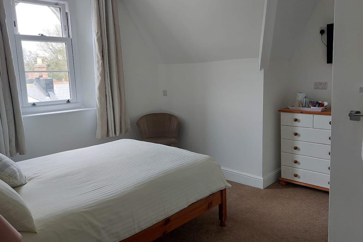 A bedroom with a bed, a chair, a dresser, and a window with curtains.