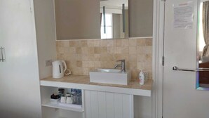 A bathroom with a white sink, a mirror, and a towel rack. There is a cabinet below the sink with toiletries. - Ashleigh House (Torquay)