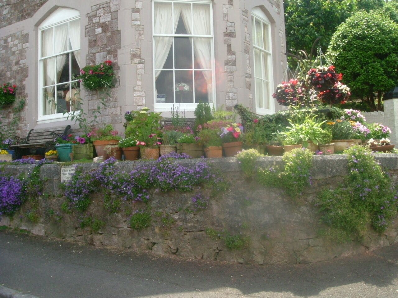 A stone building with a large window, potted plants, and a stone wall.