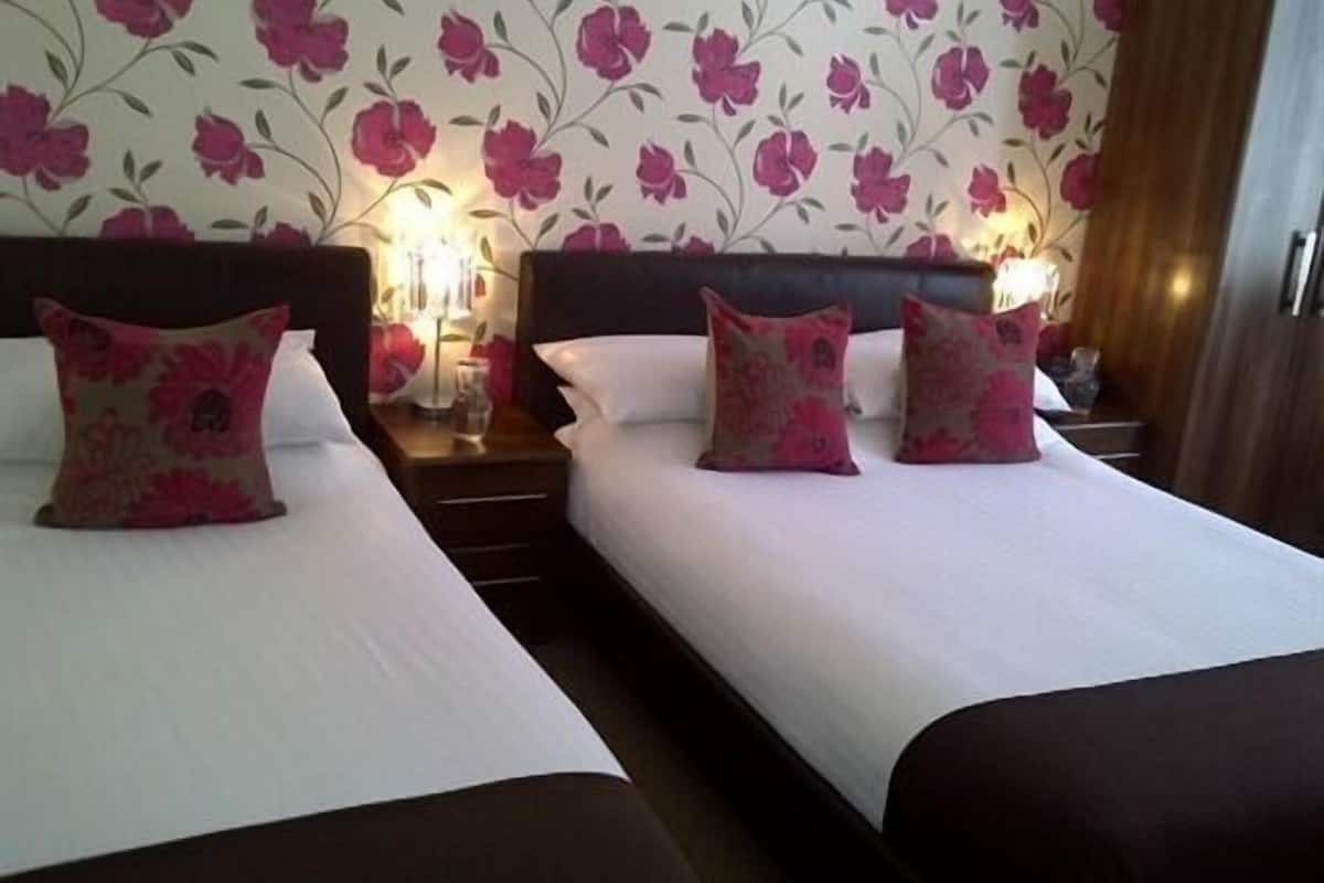 Une chambre d’hôtel avec deux lits, chacun agrémenté d’un oreiller à motifs floraux et d’une table de chevet avec une lampe.