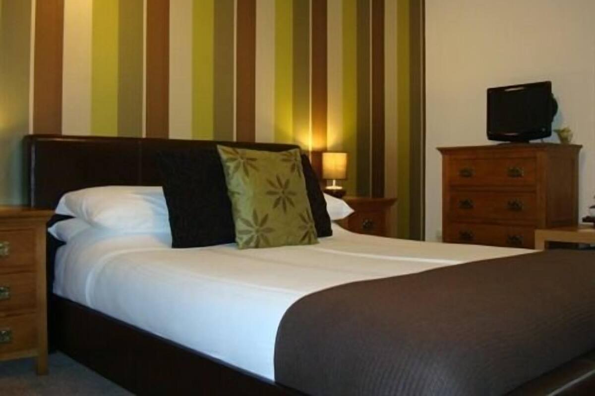Une chambre d’hôtel avec un lit, un téléviseur posé sur une commode et un mur à rayures.