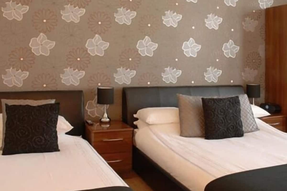Une chambre d’hôtel avec un grand lit, deux tables de chevet, une petite table et un mur orné d’un motif floral.