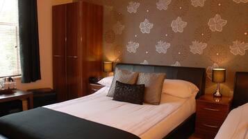 Habitación de hotel con una cama grande, un armario, una mesita de noche con lámpara y una pared con estampado floral.