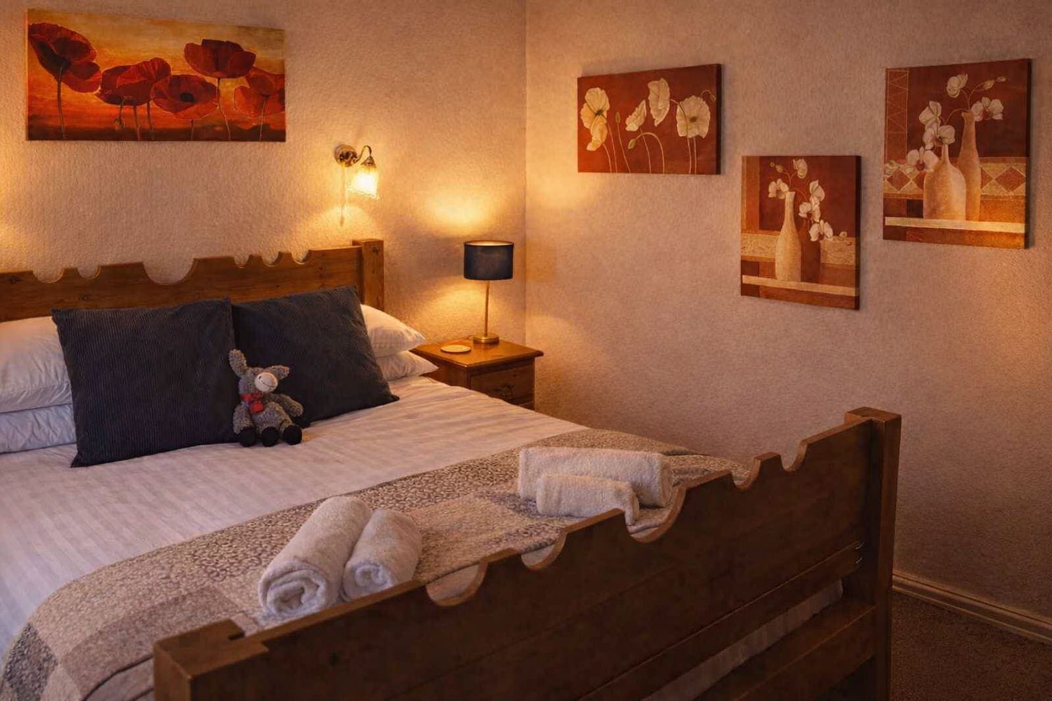 Una cama bien hecha con un cojín, una lámpara de noche y un oso de peluche.