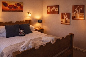 Una cama bien hecha con un cojín, una lámpara de noche y un oso de peluche.