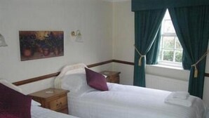 A hotel room with two single beds, a nightstand, a lamp, a painting on the wall, and a window with curtains. - The Bay Horse Country Inn (Thirsk)