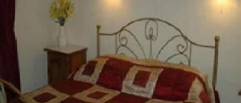 Een bed met een metalen frame en een quilt in rood en beige. Aan beide zijden van het bed bevinden zich twee wandlampen.
