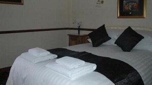 A neatly made bed with white linens and black pillows, a small wooden nightstand with a vase of flowers, and framed artwork on the walls. - The Bay Horse Country Inn (Thirsk)