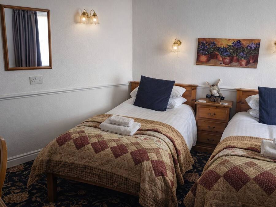 A hotel room with two beds, a wooden nightstand, a mirror, and wall-mounted lights.