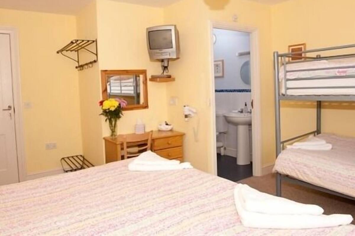 A bedroom with bunk beds, a desk with a chair, a television, and a bathroom visible through an open door.
