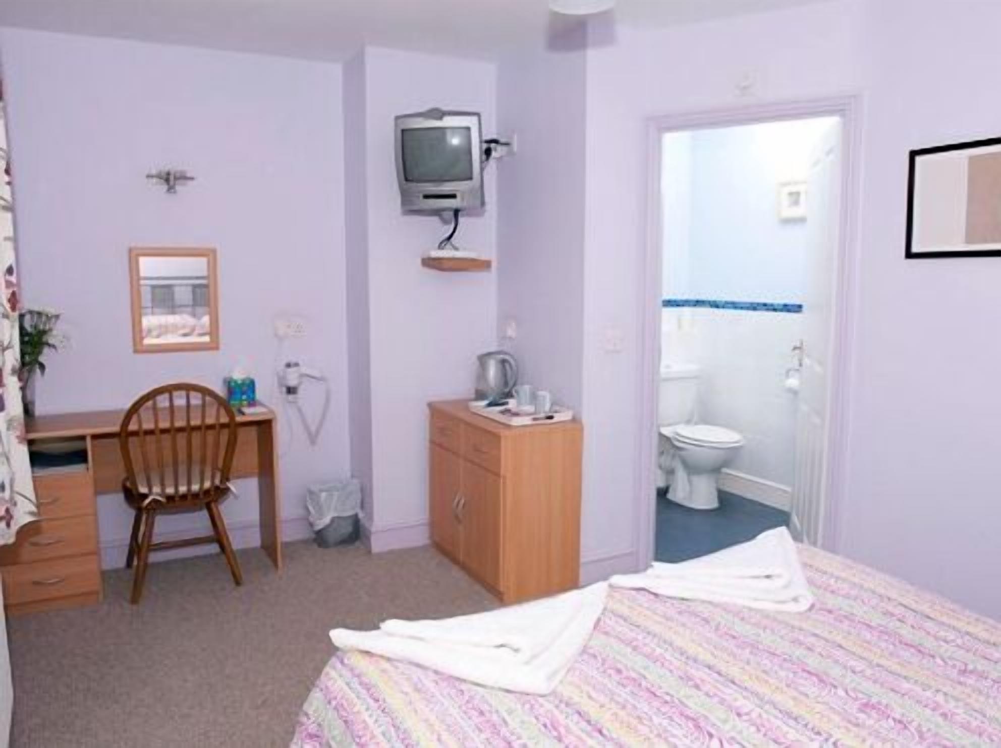 Una habitación con cama, escritorio, silla, televisor y baño.