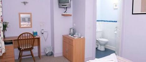Una habitación con cama, escritorio, silla, televisor y baño.