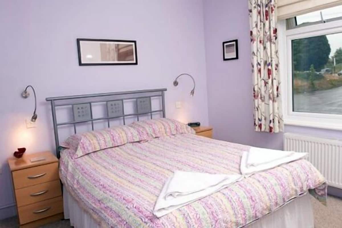 A bedroom with a bed, bedside tables, a window with curtains, and wall-mounted lights.