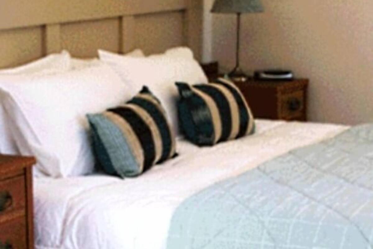 A neatly made bed with white and striped pillows, a light blue quilt, and a wooden nightstand with a lamp beside it.