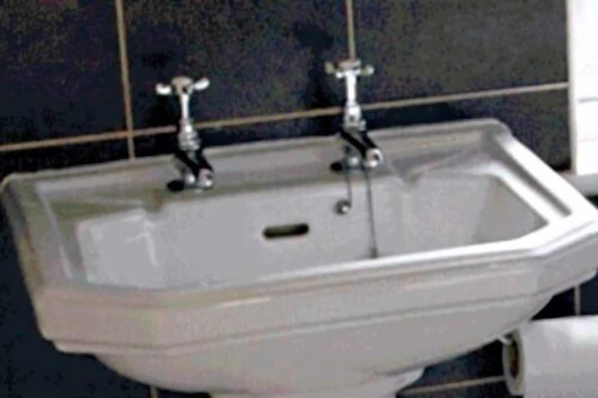 A white bathroom sink with two faucets, set against a tiled wall.