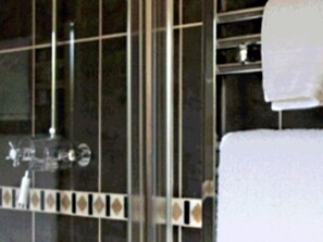 A bathroom with a glass shower enclosure, a white towel hanging on a rack, and a tiled backsplash with a decorative pattern. - The Brewers Arms (Dorchester)